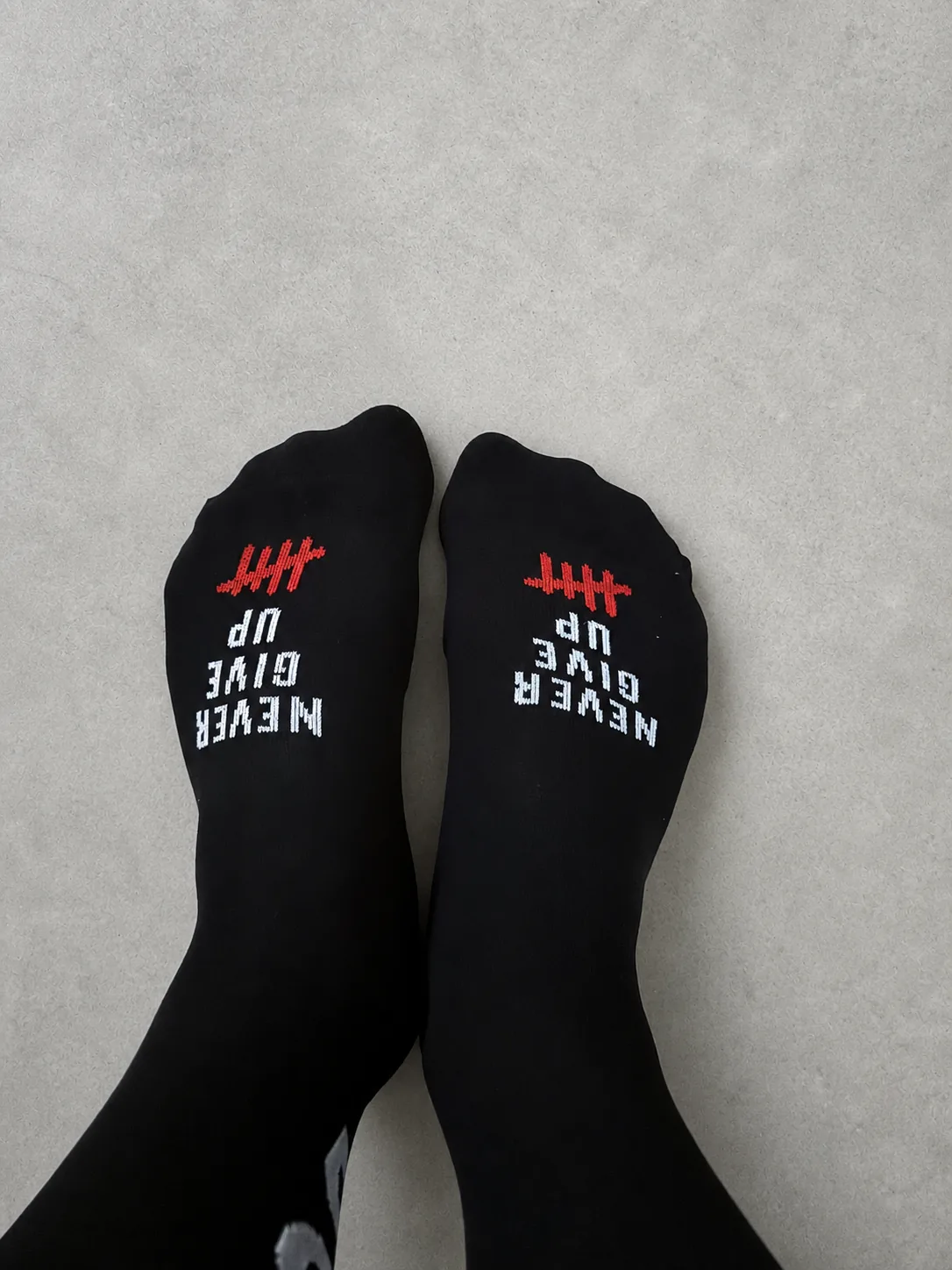 Calcetines negros de Pacific & Co. con el mensaje Never Give Up bordado en blanco sobre los dedos y un recuento de rayas en rojo