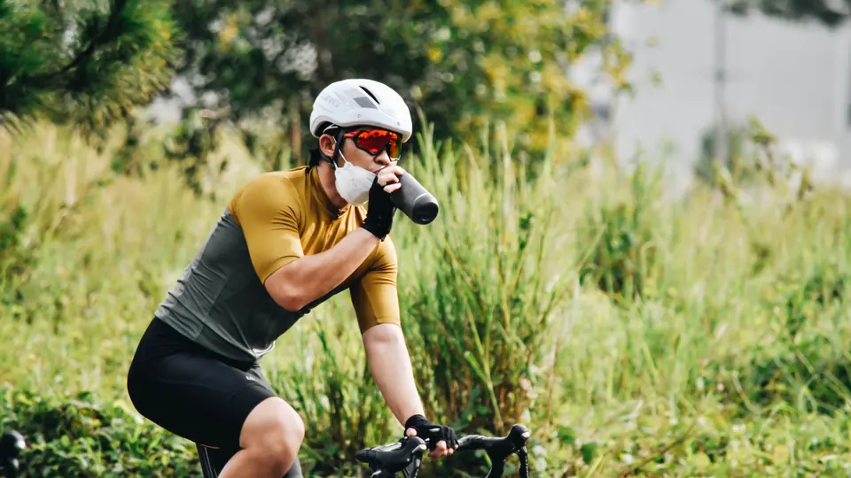 Ciclista bebiendo de su bidón mientras rueda por una carretera