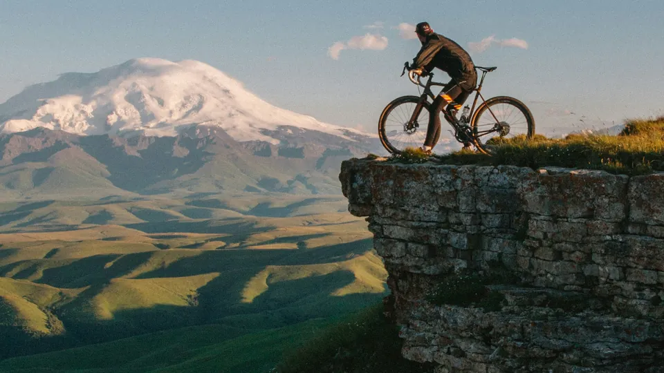 Ciclista de montaña sobre el borde de un cortado rocoso con una cordillera nevada al fondo