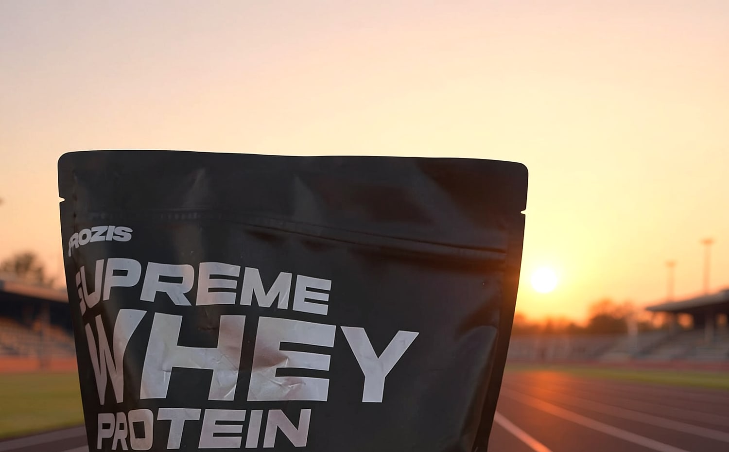 Ilustracion del envase de Supreme Whey Protein en una pista de atletismo al atardecer