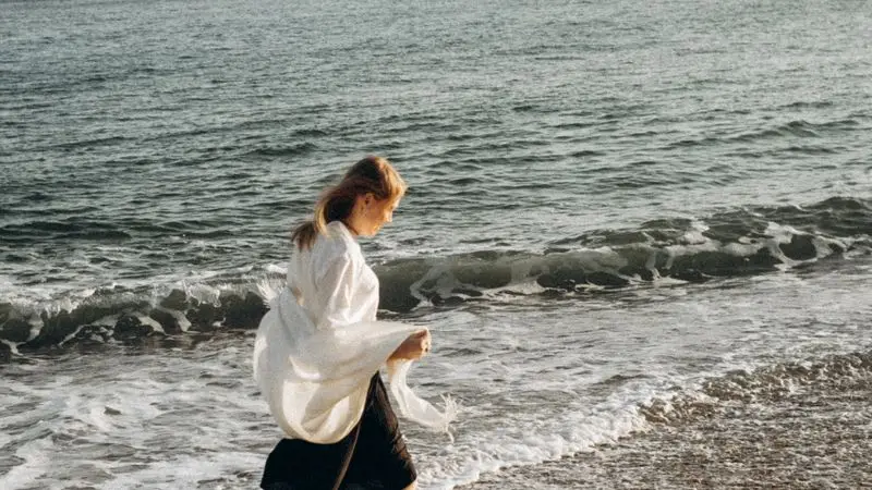 Mujer corriendo por la orilla de la playa con el mar de fondo