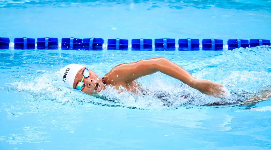 Triatleta nadando en piscina con auriculares waterproof