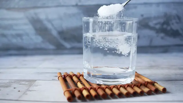 Cucharada de suplemento en polvo disolvi&eacute;ndose en un vaso de agua