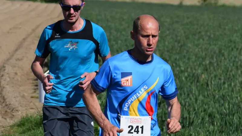 Dos corredores adultos con dorsales compitiendo en una carrera por el campo