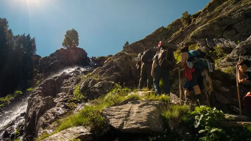 Excursionistas con mochilas subiendo por un sendero de montana rocoso