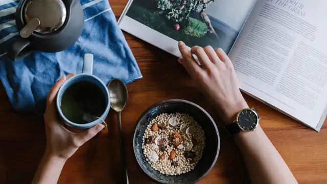 Desayuno con t&eacute; y un bol de cereales junto a un reloj de pulsera sobre una mesa de madera