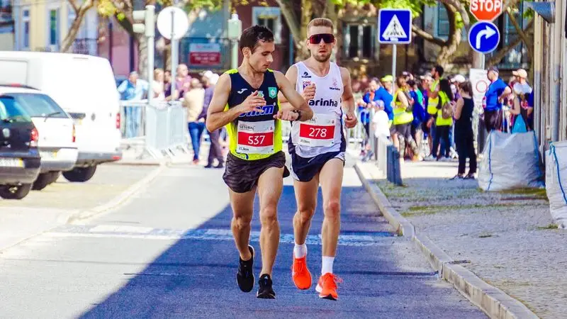 Dos corredores compitiendo en una carrera popular urbana con dorsales