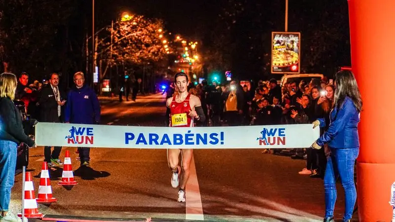 Corredor cruzando la l&iacute;nea de meta de una carrera nocturna con los brazos en alto