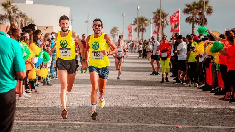 Dos corredores participando en una maraton costera con palmeras al fondo