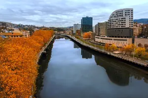 La r&iacute;a de Bilbao en oto&ntilde;o, con arbolado anaranjado y el perfil urbano al fondo