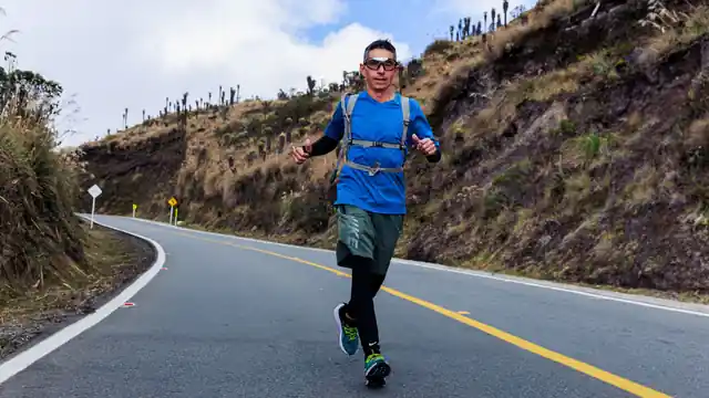 Corredor con mochila de hidrataci&oacute;n avanzando por una carretera de monta&ntilde;a