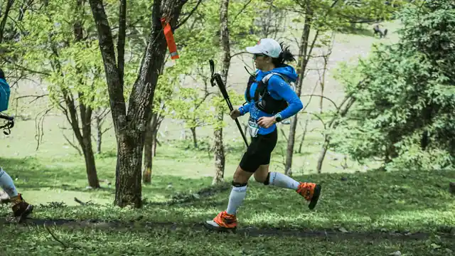 Corredora de trail avanzando con bastones por un sendero de bosque durante un entrenamiento en monta&ntilde;a