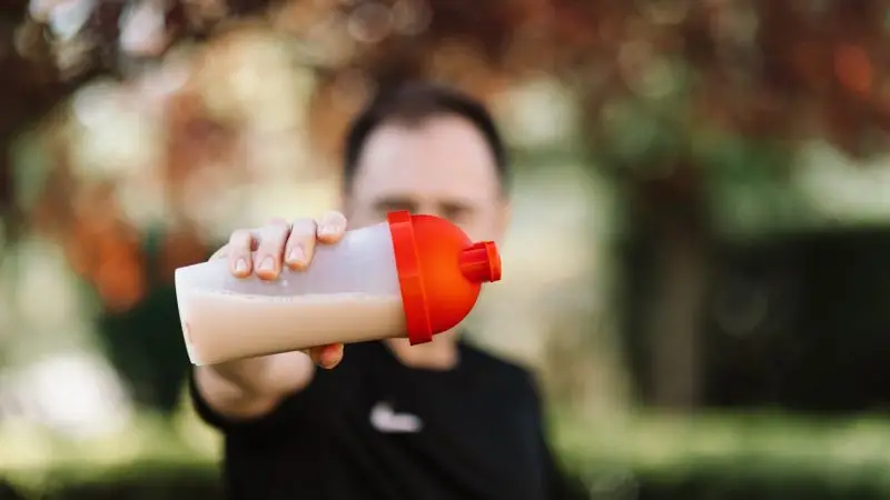 Hombre sujetando un batido de prote&iacute;nas en un vaso con tapa al aire libre