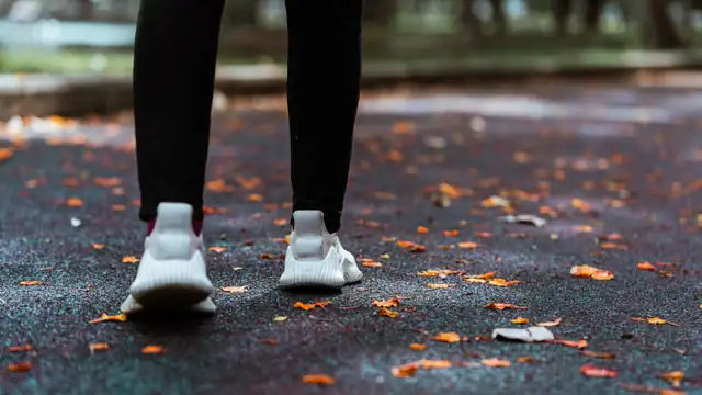 Zapatillas de running blancas sobre un camino cubierto de hojas secas