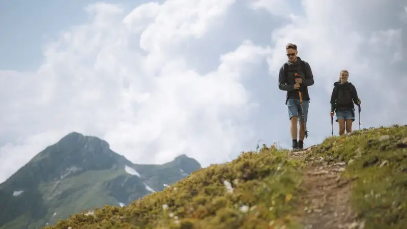 Pareja de senderistas con bastones de trekking subiendo una montaña