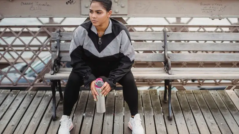 Mujer deportista sentada en un banco descansando con botella de agua despu&eacute;s de entrenar