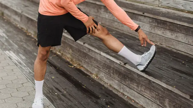 Corredor estirando el isquiotibial con el pie apoyado en unas gradas de madera despu&eacute;s de correr