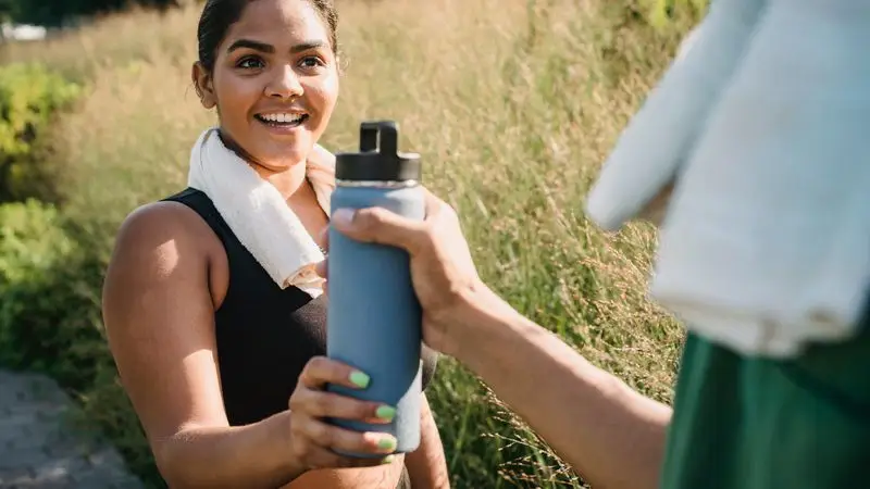 Mujer sonriente recibiendo una botella de agua durante un entrenamiento al aire libre