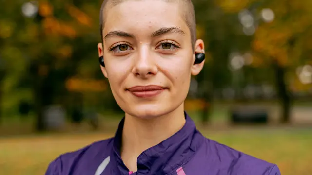 Primer plano de una deportista con auriculares in-ear colocados en ambos o&iacute;dos al aire libre