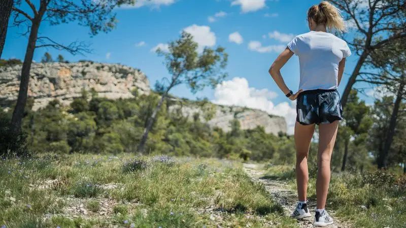 Mujer trail runner observando un paisaje de montana con acantilados rocosos