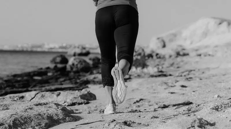 Mujer corriendo por la orilla del mar en una playa rocosa