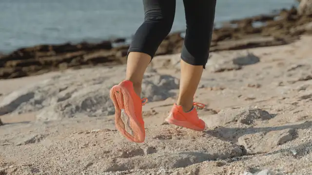 Piernas y zapatillas de una corredora avanzando por un tramo rocoso junto al mar