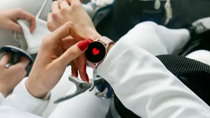 Manos ajustando un reloj deportivo en la muñeca que muestra el icono de frecuencia cardiaca