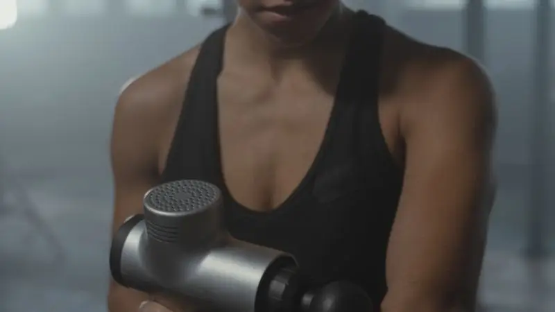Mujer usando pistola de masaje para recuperaci&oacute;n muscular