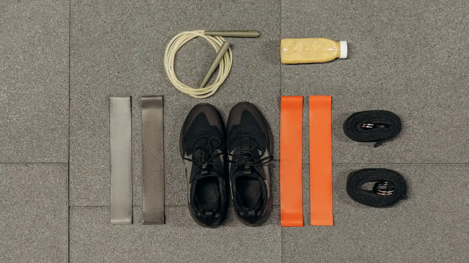 Vista cenital de equipamiento de entrenamiento ordenado sobre el suelo: zapatillas, botella, comba y bandas elásticas
