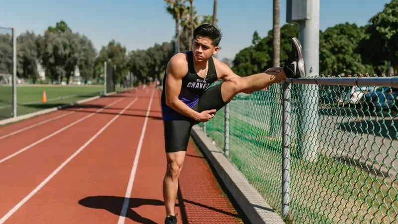 Atleta joven estirando en una pista de atletismo al aire libre en un d&iacute;a soleado