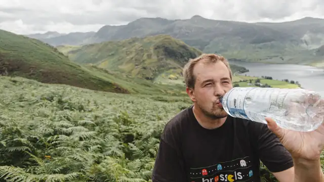 Corredor bebiendo agua de una botella en un alto del camino, con un valle de monta&ntilde;a al fondo