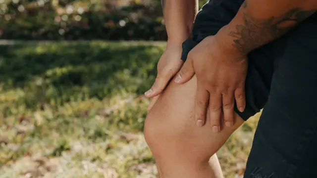 Primer plano de un deportista sujet&aacute;ndose la rodilla con ambas manos al aire libre