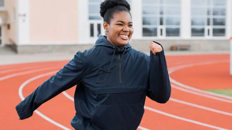 Mujer corriendo feliz en pista de atletismo al aire libre