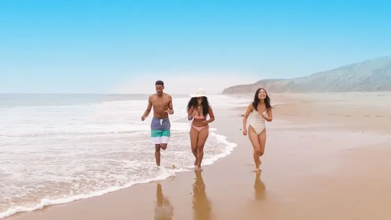 Group of friends running together on the beach outdoors