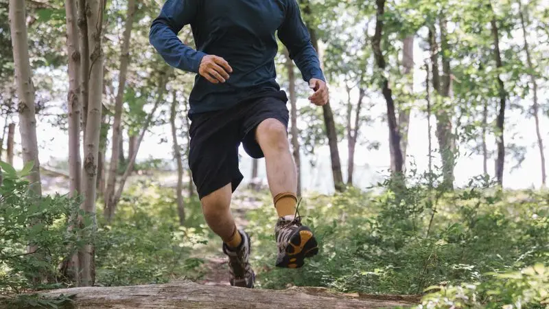 Runner saltando un obstaculo en un sendero de bosque durante un entrenamiento de trail running
