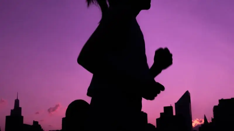 Silueta de mujer corriendo al atardecer con skyline urbano de fondo