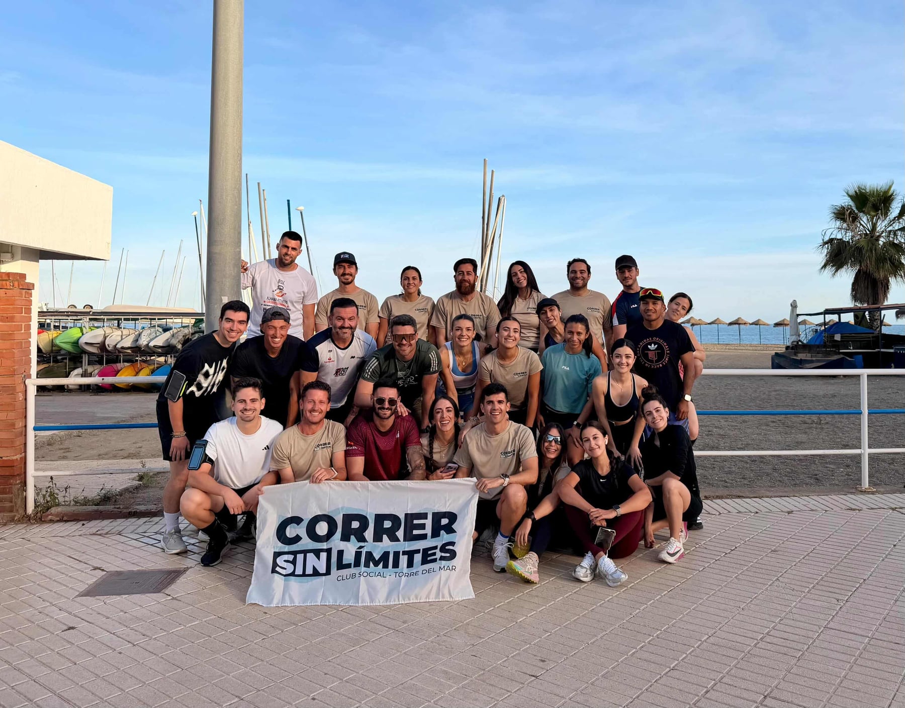 Grupo del club de running Correr Sin Límites Torre del Mar al completo en una quedada — más de 25 runners con el cartel oficial del club frente al Club Náutico y el paseo marítimo de Torre del Mar, Axarquía Málaga