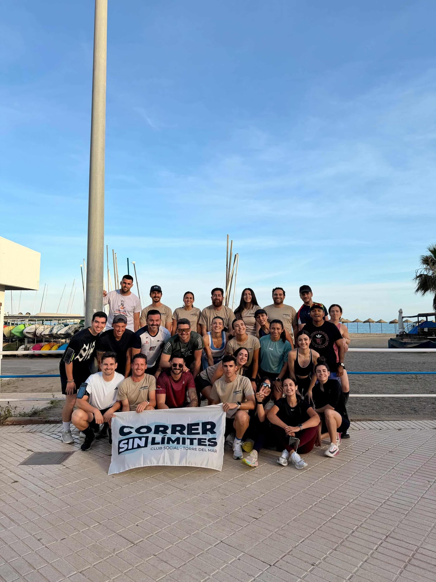 El grupo de Correr Sin Límites Torre del Mar posando con su cartel oficial tras una quedada — runners de diferentes edades y niveles frente al Club Náutico